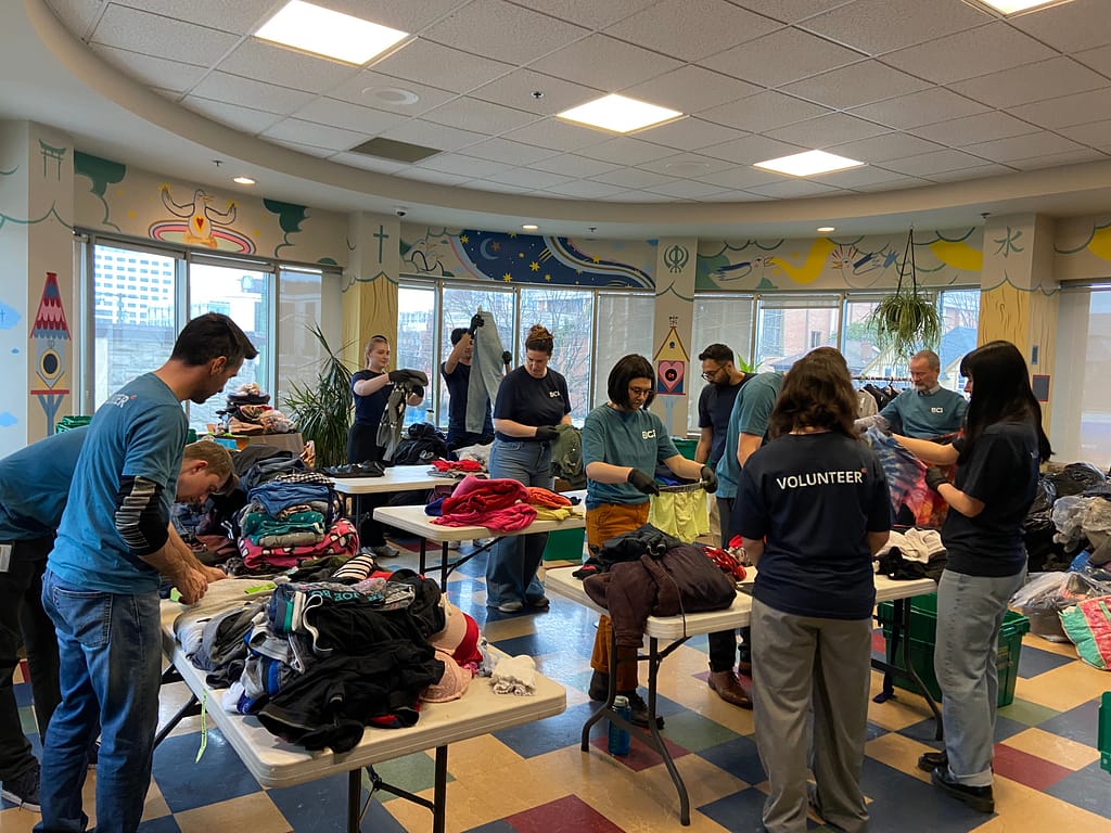 Volunteers in blue shirts sort and fold clothes in a brightly lit room with colorful decorations.