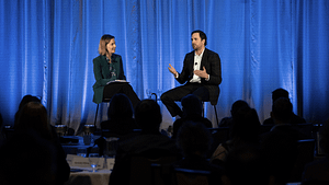 Two people on stage talking, audience in front.