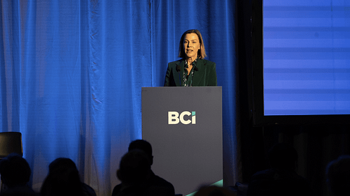 Person at BCi podium with audience and blue curtain backdrop