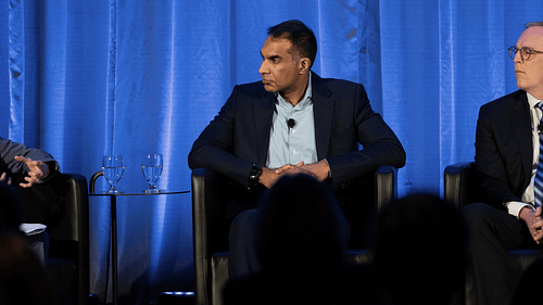 Three people seated on stage in front of a blue curtain.