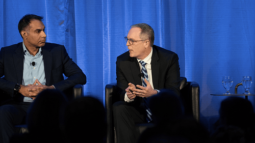 Two people seated on stage with blue curtain backdrop.