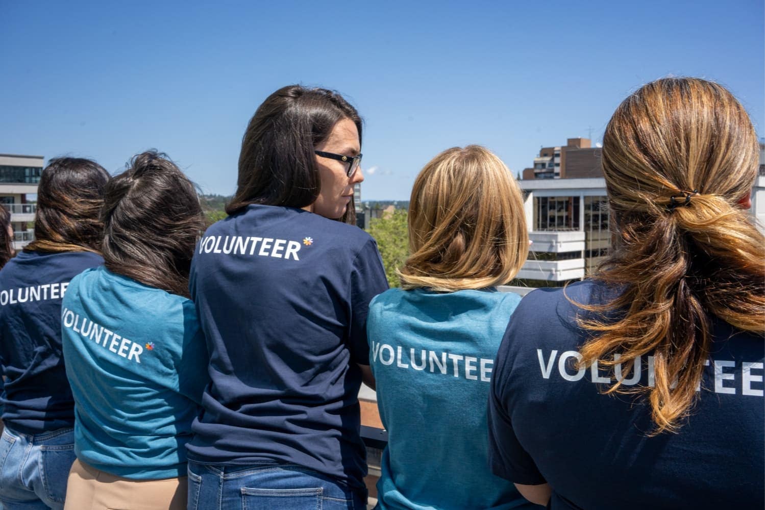 Five people outside on a balcony wearing shirts that read 'volunteer' on the back Five people outside on a balcony wearing shirts that read 'volunteer' on the back