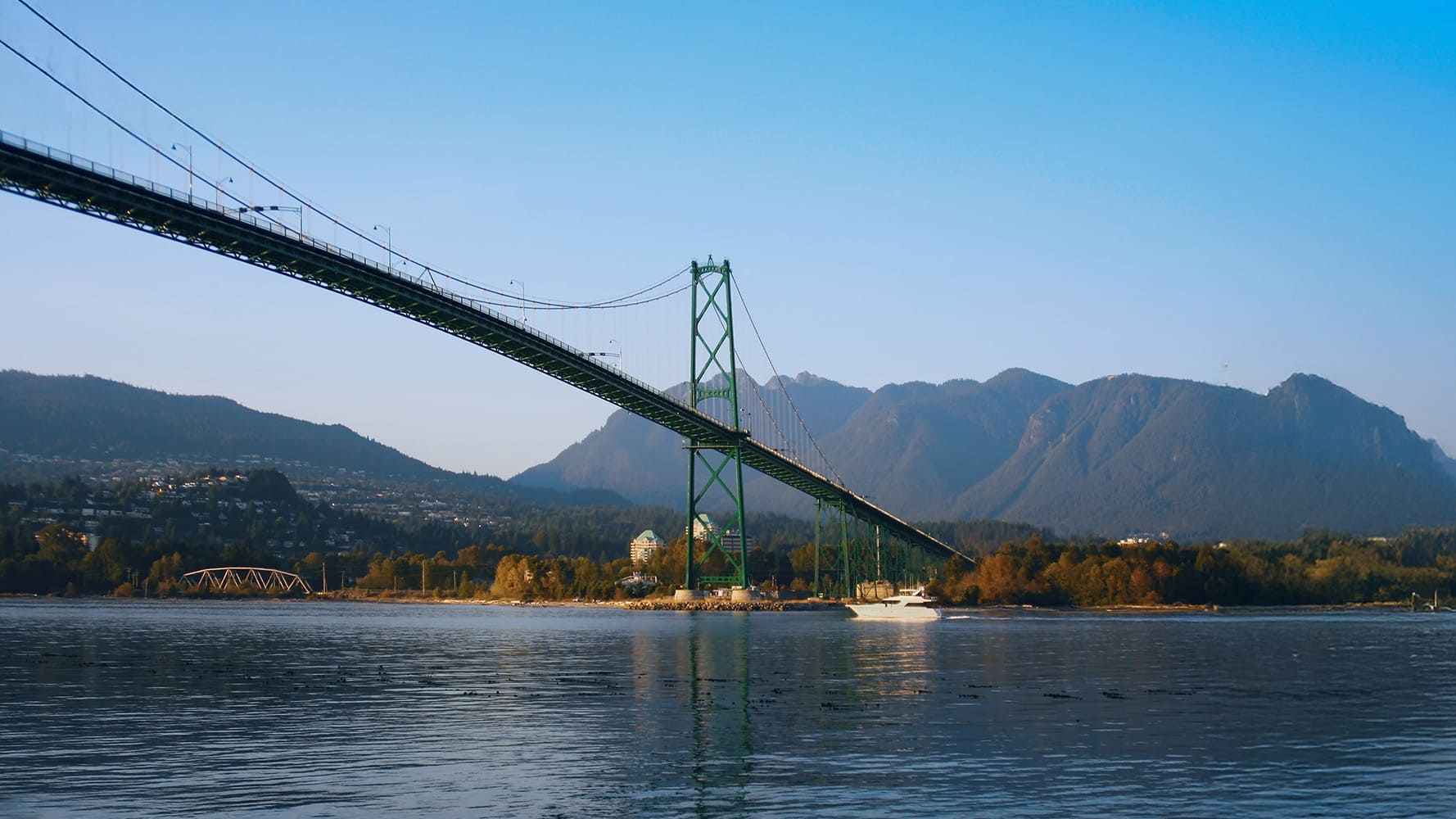 Green suspension bridge over water with mountains in the background. Green suspension bridge over water with mountains in the background.