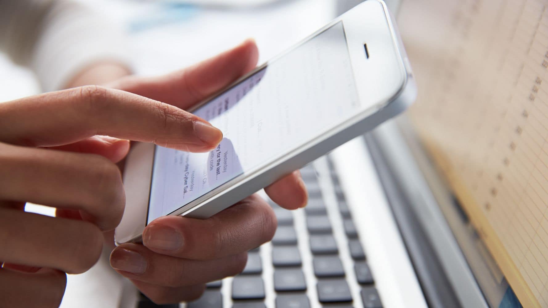 Close-up of fingers typing on phone screen with keyboard in background Close-up of fingers typing on phone screen with keyboard in background