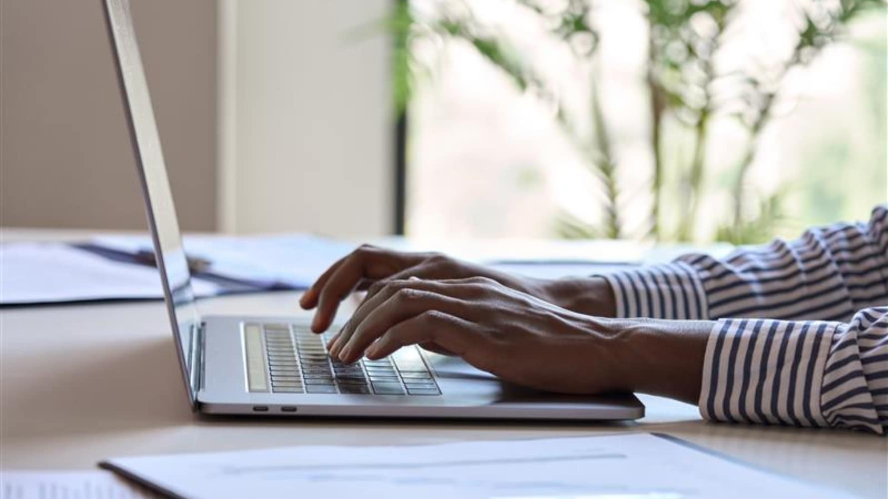 Person typing on a laptop at a desk in a bright office. Person typing on a laptop at a desk in a bright office.