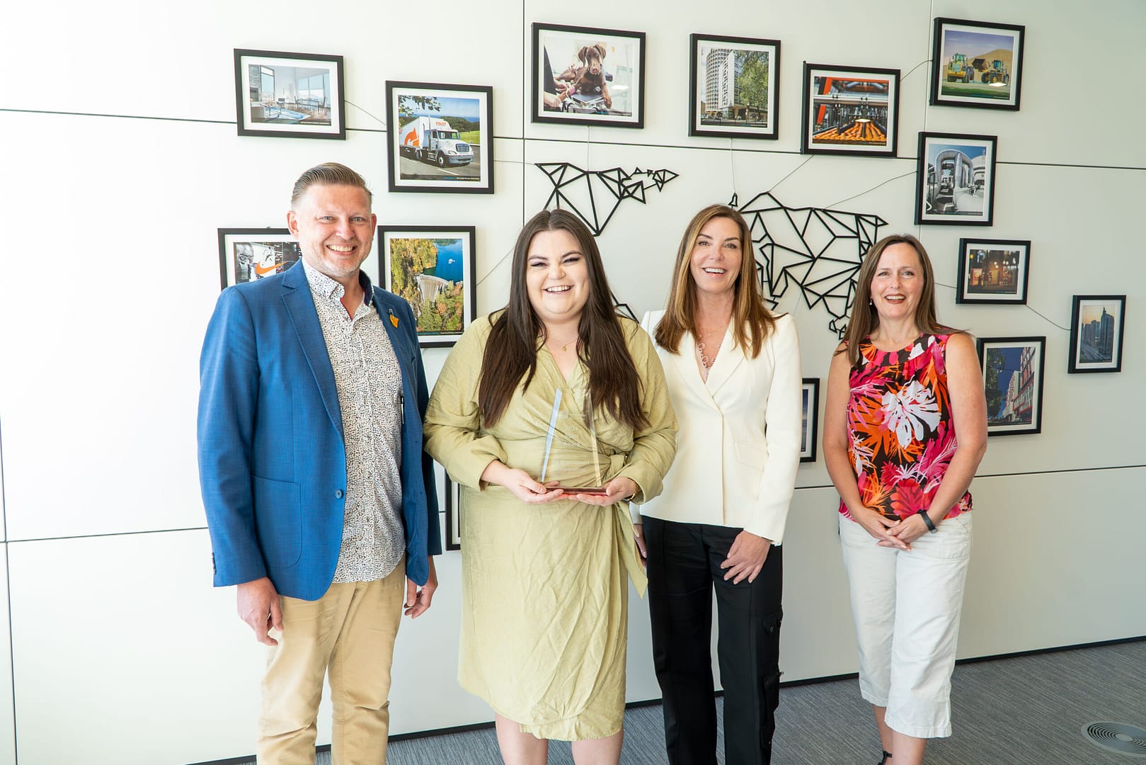 BCI's 2024 United Way Spirit Award recipients shows four people standing in front of a white wall with many framed photos on it.