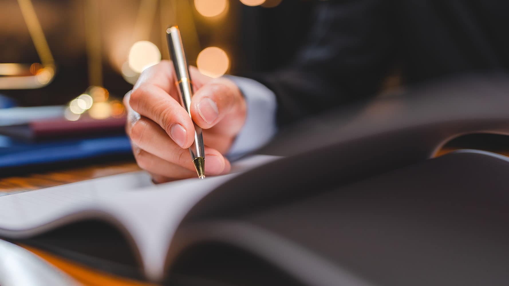 A close-up image of a person writing in a notebook with a pen.