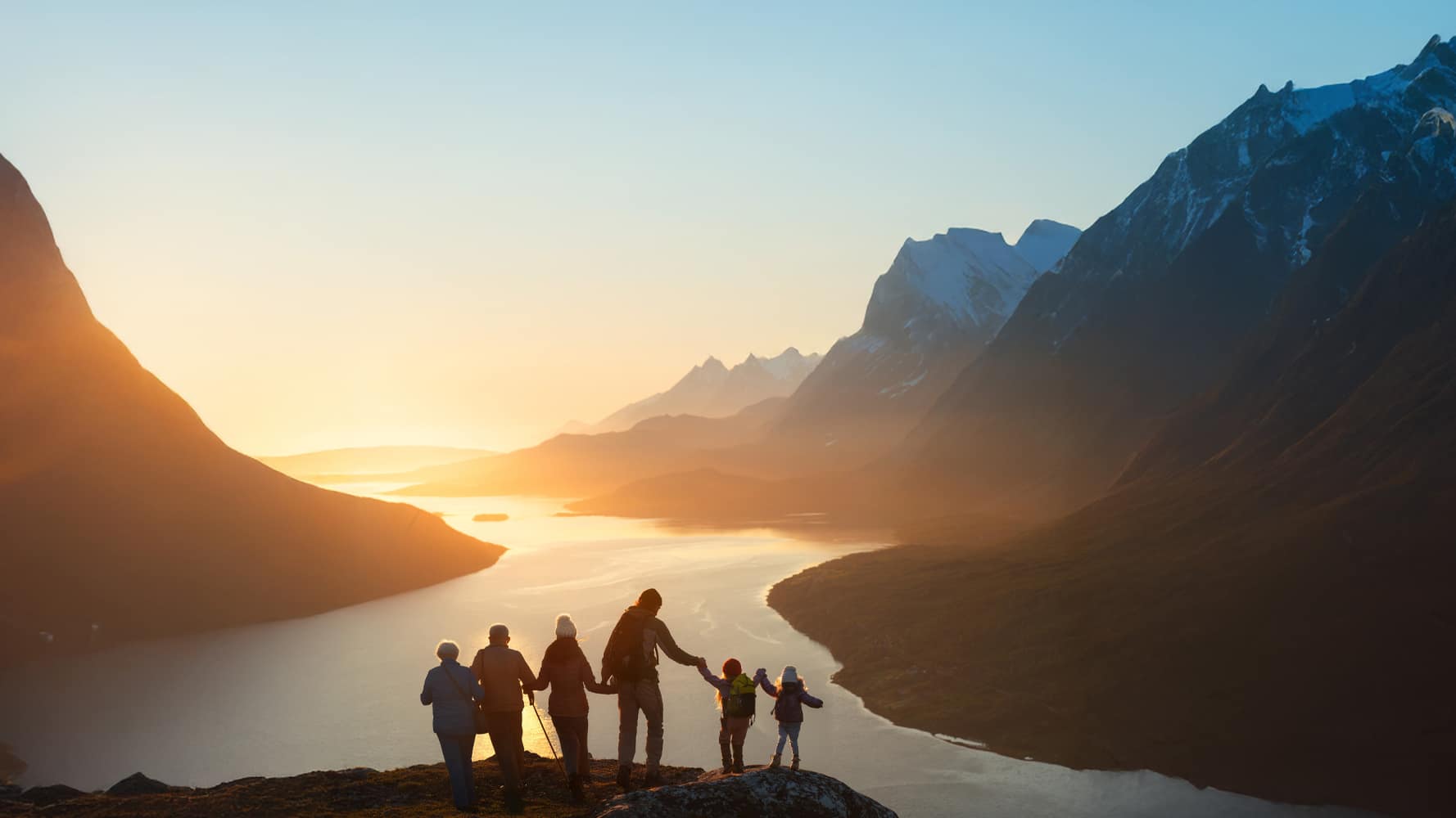 Six people holding hands on a mountain ridge at sunset, overlooking a winding river and valley.
