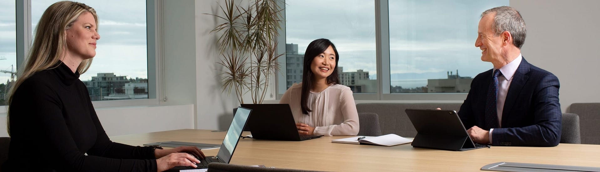 Three people in conference room working together at laptops Three people in conference room working together at laptops