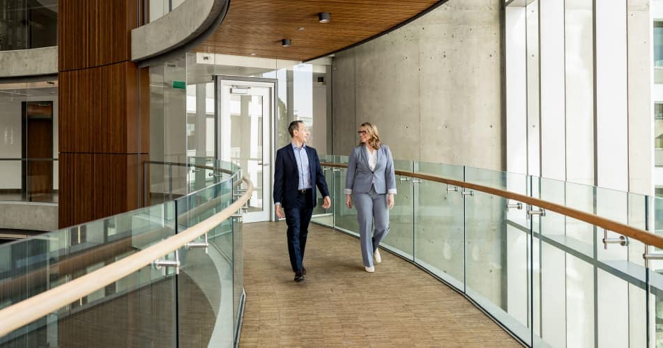 Two people walking in modern office building and smiling Two people walking in modern office building and smiling